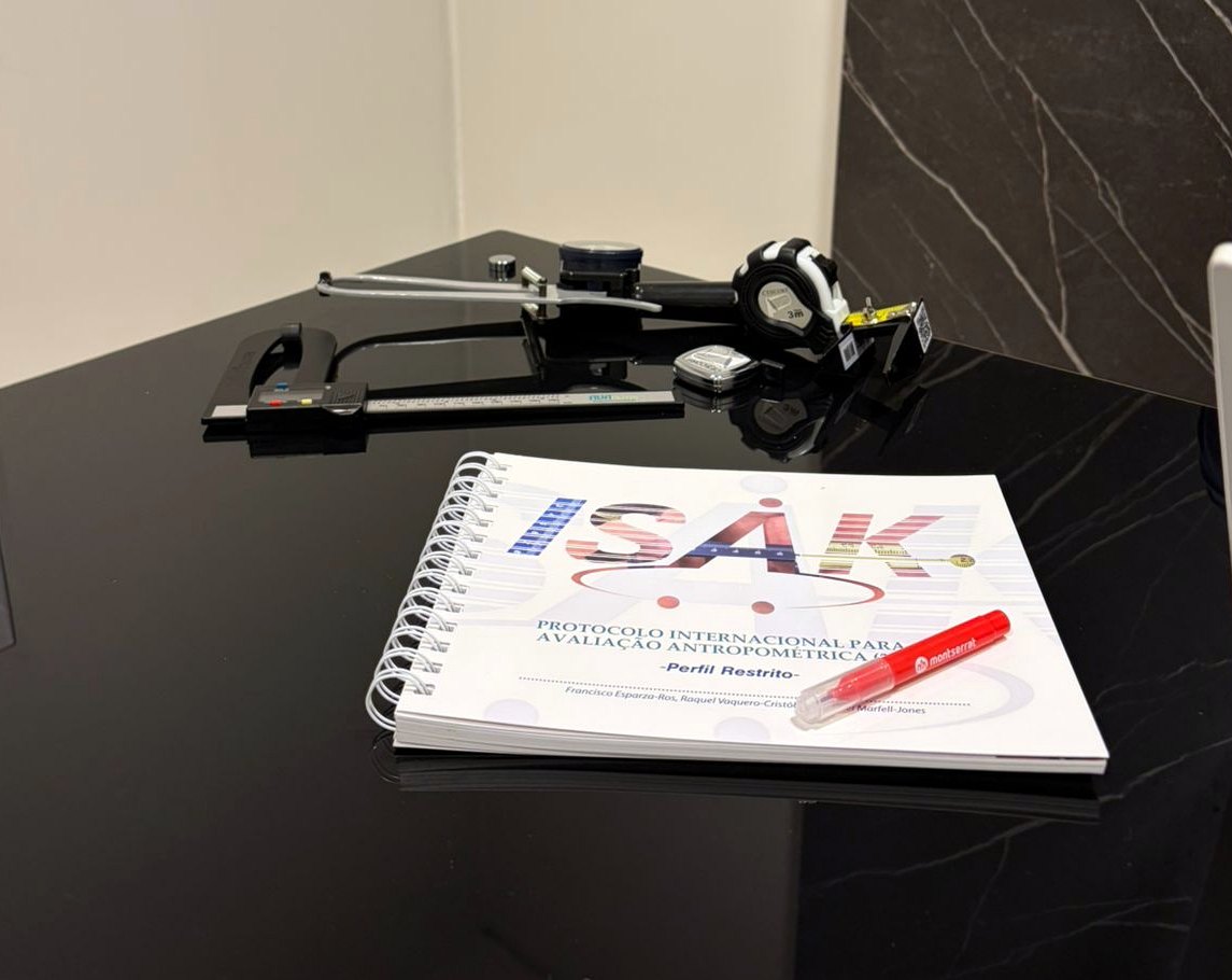 Material ISAK: protocolo de avaliação antropométrica, plicômetro e trena sobre a mesa