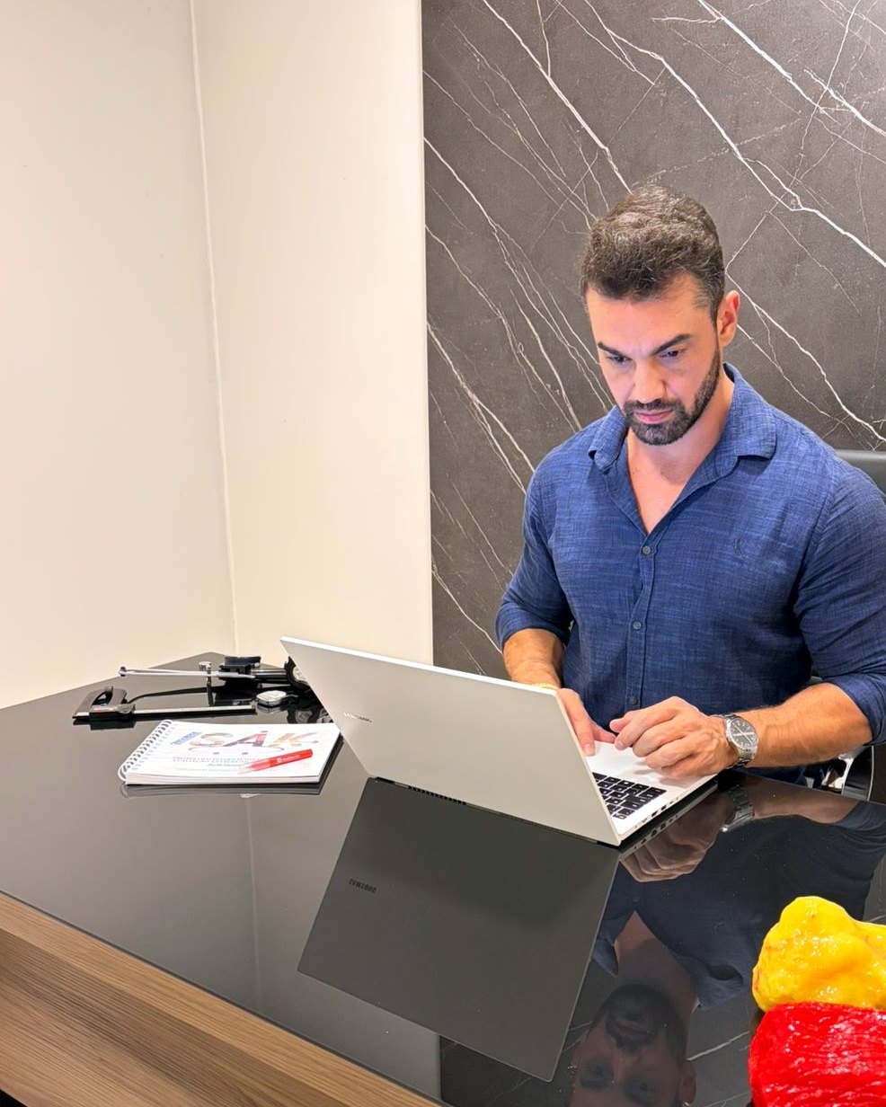 Douglas Lourenço trabalhando no notebook com material ISAK sobre a mesa